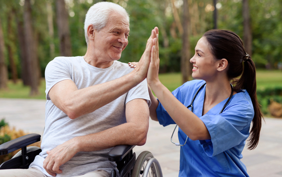 A nurse and an old man in a wheelchair high five.